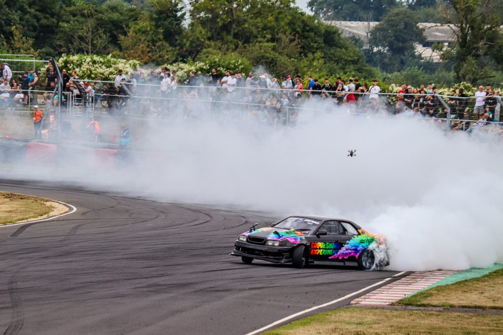 High-speed shot of a drift car on track during a UK motorsport event with drone above car and smoke coming from the tyres